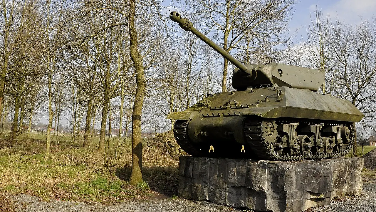 Olijfgroene M10 Wolverine-tankjager uit de Tweede Wereldoorlog op een sokkel van natuursteen aan het Canada-Poland War II Museum in Adegem, tussen kale bomen.