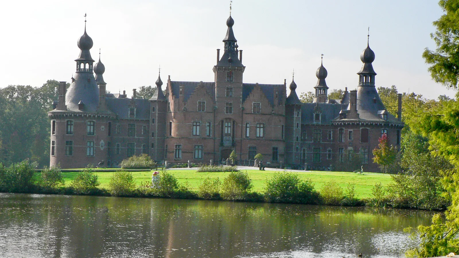 Kasteel van Ooidonk in Deinze, met rode bakstenen torens en trapgevels weerspiegeld in de slotgracht, een populaire stop op fietsroutes door het Meetjesland.