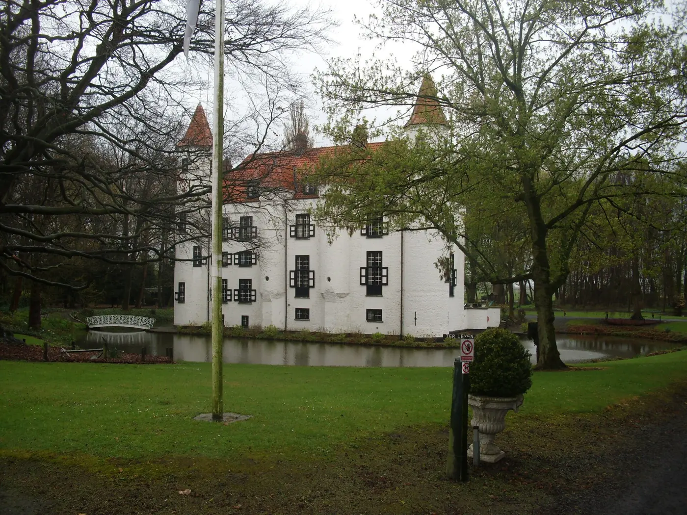Het witte Kasteel Ter Leyen in Boekhoute met trapgevels en een torentje, achter een grasveld met bomen.
